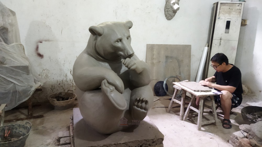 Clay model of a seated bear with artist at work
