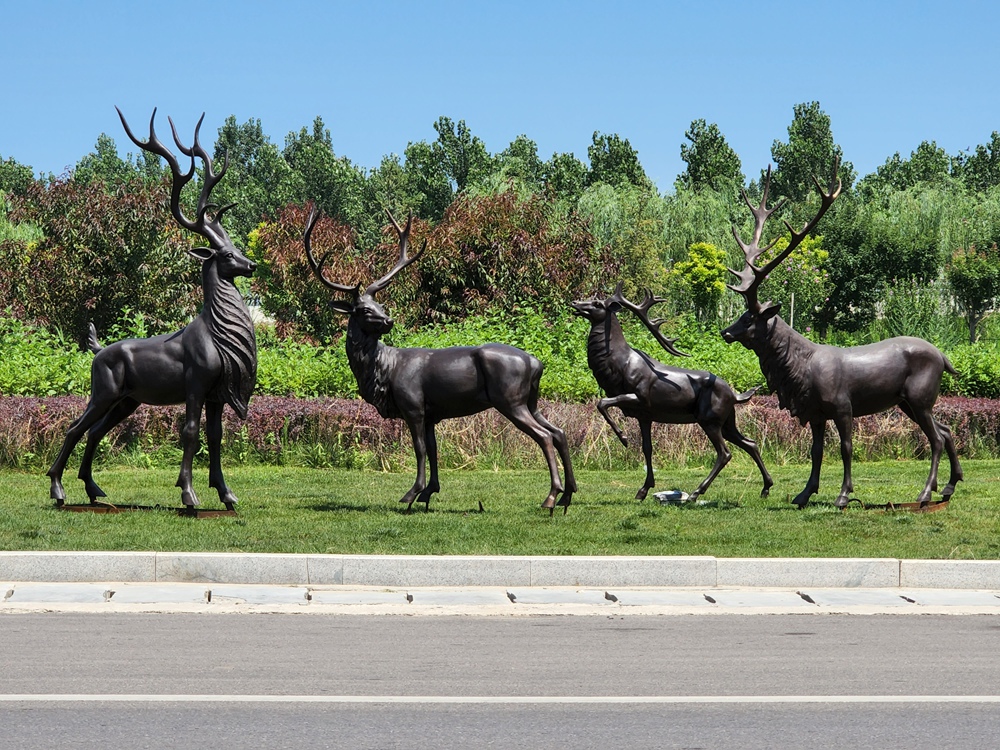 Group of bronze deer sculptures displayed on a landscaped lawn