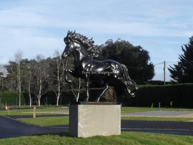 Black bronze trotting horse sculpture on an outdoor pedestal